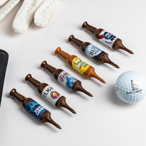 Pu&ograve; includere: Cinque tee da golf in plastica marrone a forma di bottiglie di birra in miniatura con varie etichette colorate, una pallina da golf bianca con la scritta Putt Light, un'impugnatura per mazza da golf nera testurizzata e un guanto da golf in pelle.
