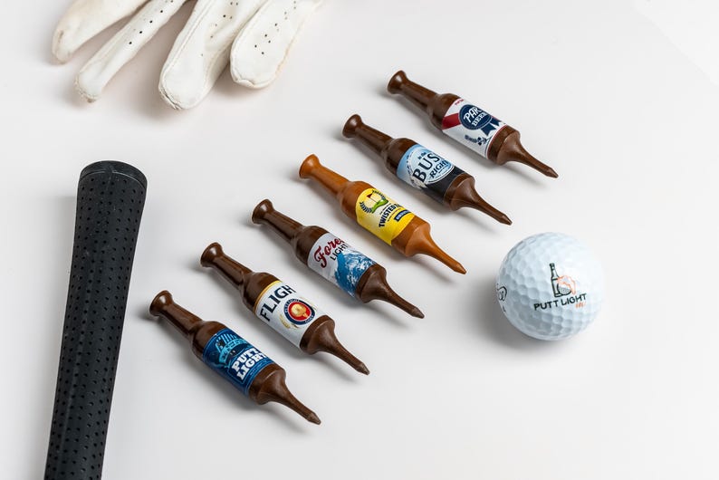 Pu&ograve; includere: Cinque tee da golf in plastica marrone a forma di bottiglie di birra in miniatura con varie etichette colorate, una pallina da golf bianca con la scritta Putt Light, un'impugnatura per mazza da golf nera testurizzata e un guanto da golf in pelle.