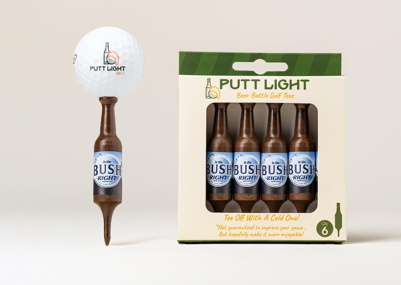 Pu&ograve; includere: Una pallina da golf bianca con il logo Putt Light &egrave; posizionata sopra un tee da golf marrone a forma di bottiglia di birra. Accanto c'&egrave; una scatola di cartone contenente quattro tee da golf marroni identici, etichettati Putt Light Beer Bottle Golf Tees.