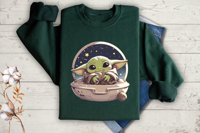 Puede incluir: Una sudadera verde oscuro con un gr&aacute;fico de un personaje alien&iacute;gena verde en una nave espacial contra un fondo de cielo nocturno estrellado.