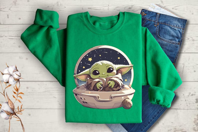 Puede incluir: Sudadera verde con una imagen de dibujos animados de un personaje alien&iacute;gena verde en una nave espacial. El extraterrestre sonr&iacute;e y tiene ojos grandes. La nave espacial est&aacute; rodeada de estrellas.
