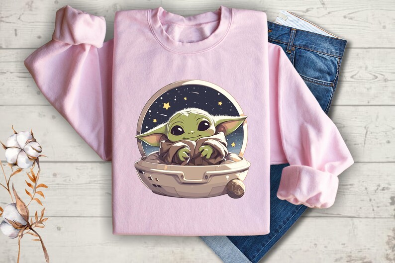 Puede incluir: Sudadera rosa con un gr&aacute;fico de un personaje alien&iacute;gena verde en una nave espacial sobre un fondo estrellado.