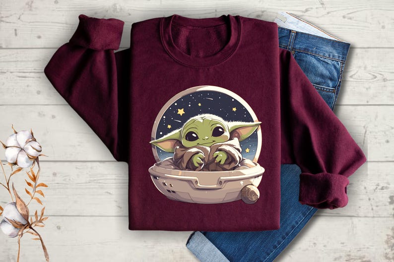 Puede incluir: Sudadera color burdeos con un gr&aacute;fico de un personaje alien&iacute;gena verde en una nave espacial. El personaje est&aacute; sentado en la nave espacial con los brazos cruzados y tiene una expresi&oacute;n linda en su rostro.