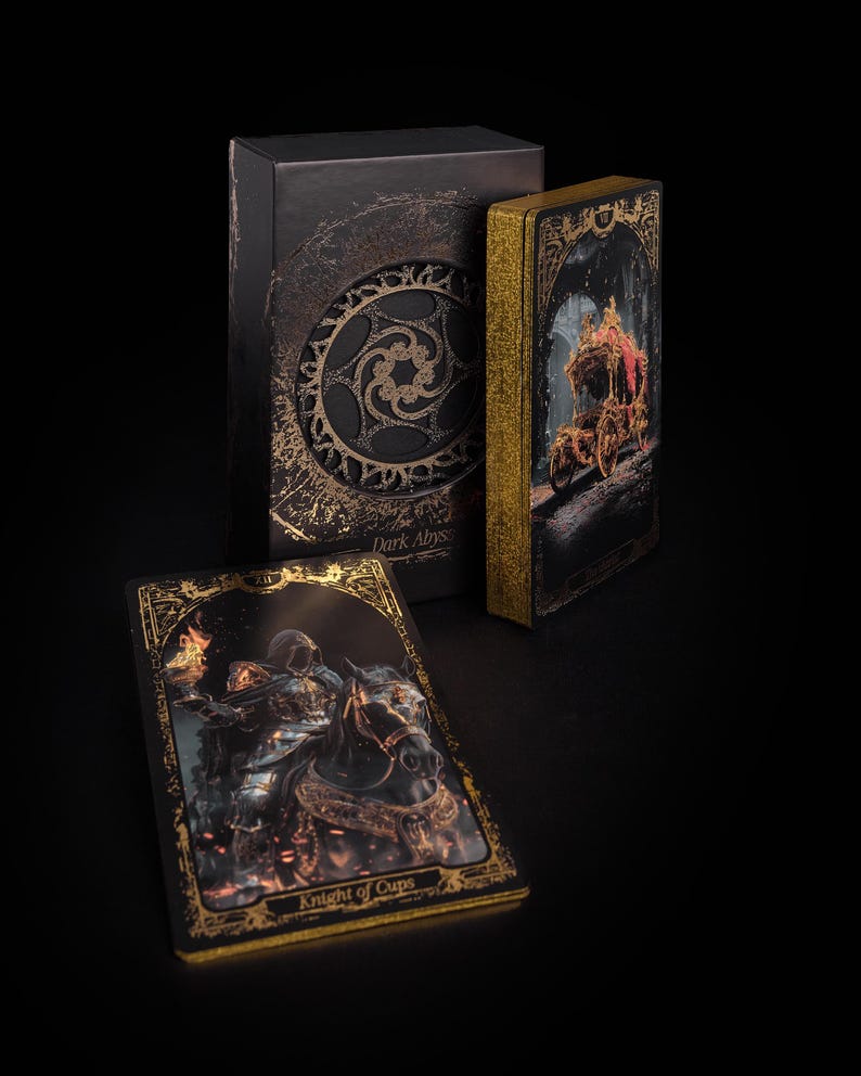 May include: A tarot card deck with a dark aesthetic. The box and cards feature gold accents and intricate designs. One card shows a knight on horseback, labeled "Knight of Cups." The deck is titled "Dark Abyss."
