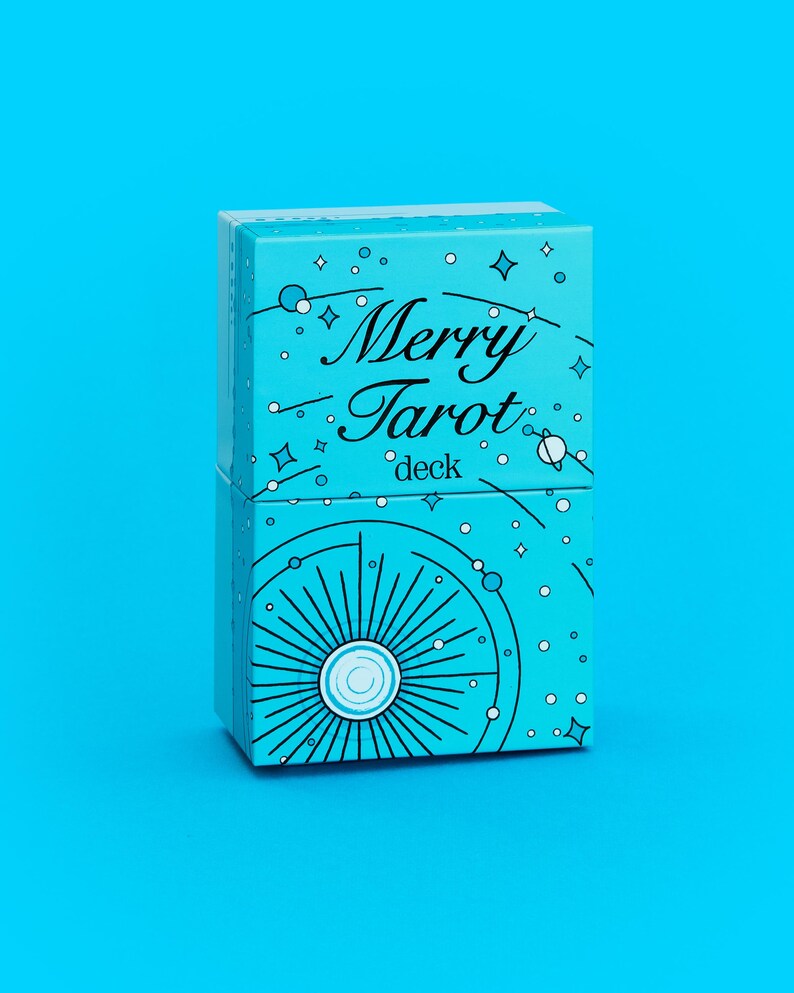 Może przedstawiać: Turkusowe pudełko na talię kart tarota z napisem "Merry Tarot deck" w ozdobnej czcionce. Pudełko jest ozdobione białymi gwiazdami, kropkami i niebiańskim wzorem. Tło jest w jednolitym turkusowym kolorze.