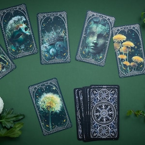May include: A set of rectangular tarot cards featuring dark, moody illustrations of yellow dandelions, a human face, and celestial patterns. The cards are arranged in a spread with one deck stacked, surrounded by white chrysanthemum flowers and green leaves.