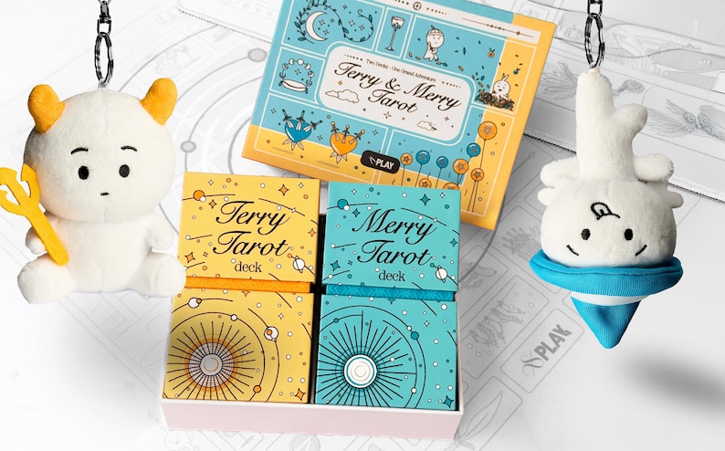 Może przedstawiać: Zestaw kart tarota z pasującą pluszową zabawką. Zestaw zawiera dwie talie z napisami "Terry Tarot" i "Merry Tarot", przewodnik i dwie pluszowe zabawki. Talie znajdują się w r&oacute;żowym pudełku. Pluszowe zabawki są białe z ż&oacute;łtymi i niebieskimi akcentami.
