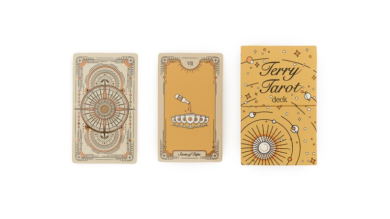 May include: A tarot card deck with three visible elements. Two cards and a box are displayed. The cards have beige and orange designs. The box is gold with the text "Terry Tarot deck". The cards have intricate line art.