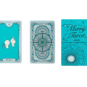 Może przedstawiać: Turkusowa talia Merry Tarot z dwiema kartami tarota i pudełkiem. Karty mają turkusowe tło z białymi i turkusowymi ilustracjami. Na pudełku widnieje napis "Merry Tarot deck" w białym kolorze.