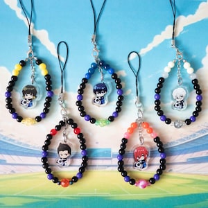 May include: Six colourful beaded phone charms featuring anime characters. Each charm depicts a different character with black hair and a white shirt. The charms are made with black, blue, yellow, white, and red beads.