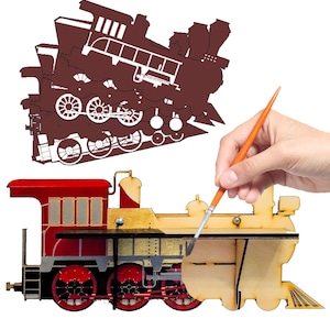 May include: A wooden train engine model with red, gold, and black paint. A hand is holding a paintbrush and painting the engine. The engine is being painted to match a brown silhouette of a train engine.