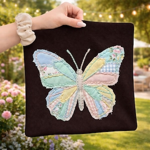 May include: A dark brown square fabric pouch featuring a large butterfly appliqué made from various pastel-colored fabric patches. The butterfly wings include light blue, yellow, pink, and floral patterns with visible stitching along the edges.
