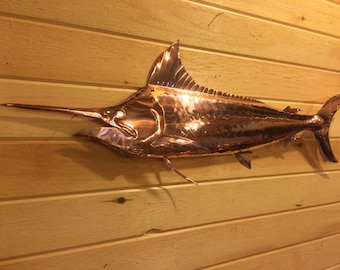 May include: A copper marlin wall sculpture with a hammered finish. The marlin is depicted in a realistic pose with its fins and tail spread out.