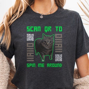 May include: Dark heather grey t-shirt with a green pixelated design featuring a cat and the text "SCAN QR TO DIAL" and "SPIN ME AROUND".