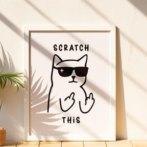 以下が含まれることがあります： サングラスをかけた猫が中指を立てている白黒イラストの、白いフレームに入ったアートプリント。「SCRATCH THIS」の文字が猫の上と下に印刷されています。