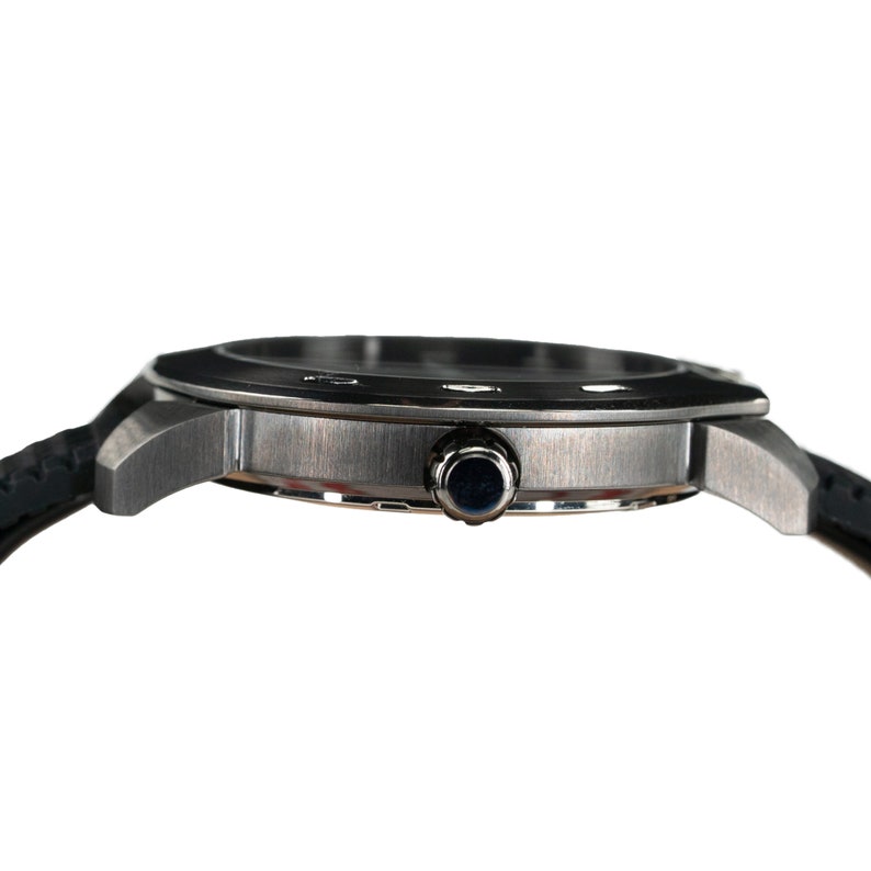 May include: A silver-toned wristwatch with a black rubber band. The watch has a round face with a silver bezel and a black dial.
