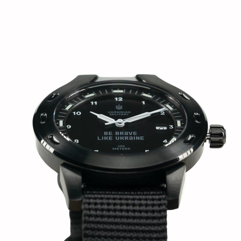May include: A black wristwatch with a black nylon strap. The watch face is black with white markings and the text "BE BRAVE LIKE UKRAINE" and "UKRAINIAN MILITARY". The watch is water resistant to 100 meters.