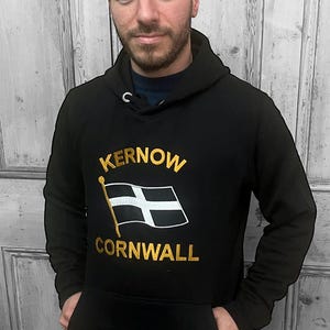 May include: Black hooded sweatshirt with a gold embroidered design featuring the text "Kernow Cornwall" and a white and black flag.