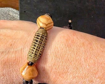 Bracelet noeud en cuir fait main avec une perle en bronze unique en son genre flanquée de deux perles en bois. Fermeture réglable par nœud cylindrique.