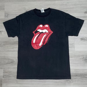 May include: Black t-shirt featuring the iconic red and white Rolling Stones tongue and lips logo. The graphic is centered on the front of the shirt. The shirt has a crew neck and short sleeves. The fabric appears to be cotton.