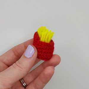 May include: A small, red crocheted container filled with yellow crocheted french fries.