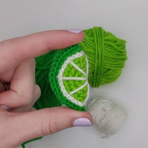 May include: A green crocheted lime with a white crocheted slice, along with green and white yarn balls.