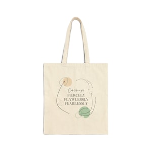 May include: A beige tote bag with black text that reads "Code like a girl: Fiercely, Flawlessly, Fearlessly". The text is surrounded by black lines and abstract shapes in beige and green.
