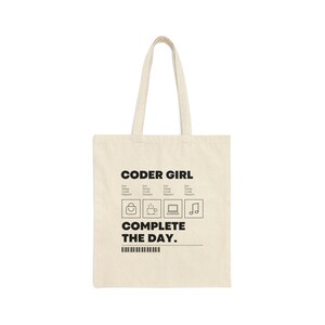 May include: A beige tote bag with the text "CODER GIRL" and a graphic of four icons: a purse, a cup of coffee, a laptop, and a musical note. The text "COMPLETE THE DAY." is below the icons.