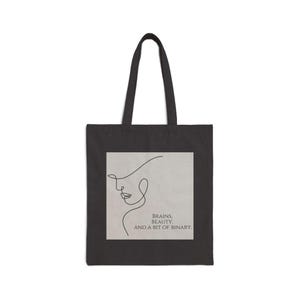 Può includere: Borsa tote nera con un disegno a linea bianca di un viso femminile e il testo "Brains, Beauty, and a bit of binary."
