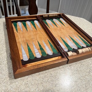 May include: A wooden backgammon game set with a green and white playing surface. The set is open and the playing pieces are visible.