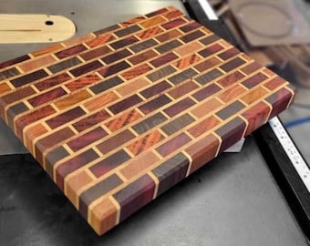May include: A rectangular wooden cutting board with a brick pattern made from different types of wood. The wood has a variety of colors, including purple, brown, red, and yellow.