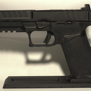 May include: A black handgun with a textured grip and a rail system on the bottom. The gun is resting on a black stand. The slide has angled grooves and a raised sight.