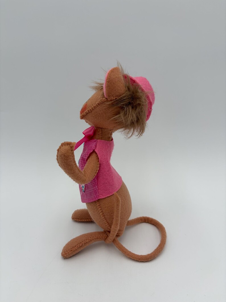 May include: A handmade brown mouse doll wearing a pink vest and hat. The mouse has brown fur and a long tail. The pink vest has a small checkered pattern. The hat has a brown fur trim and a pink ribbon.