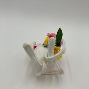 K&ouml;nnte beinhalten: Wei&szlig;e Filzspinne mit gelben und rosa Bl&uuml;ten und gr&uuml;nen Bl&auml;ttern oben.
