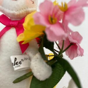 K&ouml;nnte beinhalten: Ein wei&szlig;er Pl&uuml;schhase h&auml;lt einen Strau&szlig; rosa und gelber Blumen. Der Hase hat eine rosa Schleife um den Hals und ein Etikett mit der Aufschrift "Lee @2013".