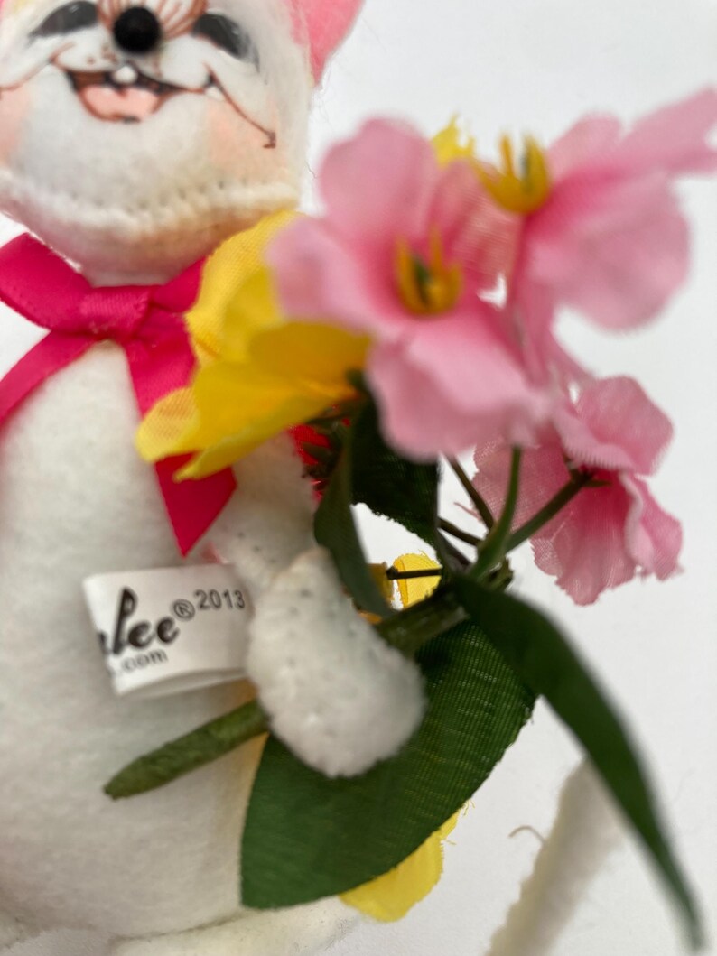 K&ouml;nnte beinhalten: Ein wei&szlig;er Pl&uuml;schhase h&auml;lt einen Strau&szlig; rosa und gelber Blumen. Der Hase hat eine rosa Schleife um den Hals und ein Etikett mit der Aufschrift "Lee @2013".