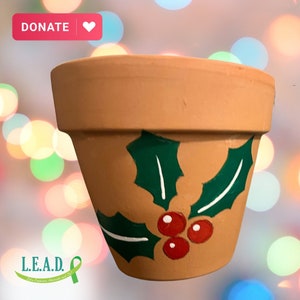 May include: A terracotta flower pot with a painted design of holly leaves and red berries. The pot is decorated with green and white paint.