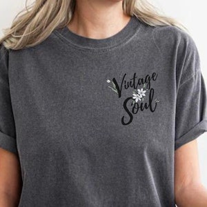 May include: A dark gray t-shirt with a vintage soul graphic featuring white flowers and green leaves.