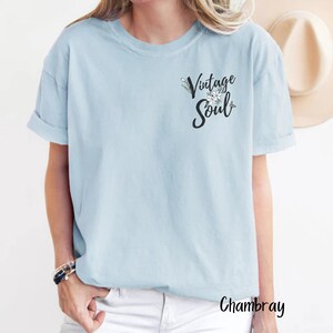 May include: A light blue t-shirt with the text "Vintage Soul" in black lettering with a floral design. The shirt is made of a soft, comfortable chambray fabric.