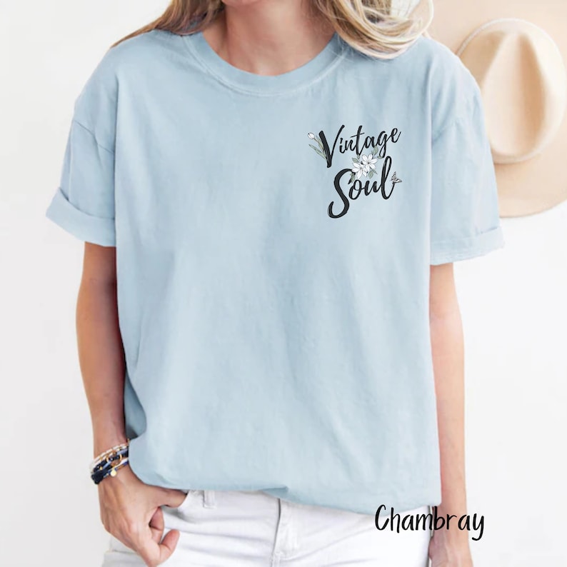 May include: A light blue t-shirt with the text "Vintage Soul" in black lettering with a floral design. The shirt is made of a soft, comfortable chambray fabric.