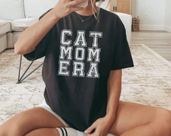 Könnte beinhalten: Schwarzes T-Shirt mit dem Aufdruck "CAT MOM ERA" in Weiß auf der Vorderseite.