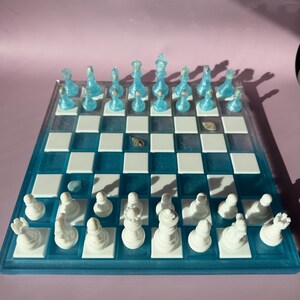 May include: A handcrafted chess set with a blue and white board. The chess pieces are white and blue. The board is square with alternating white and blue squares. The chess set is a unique and decorative item.