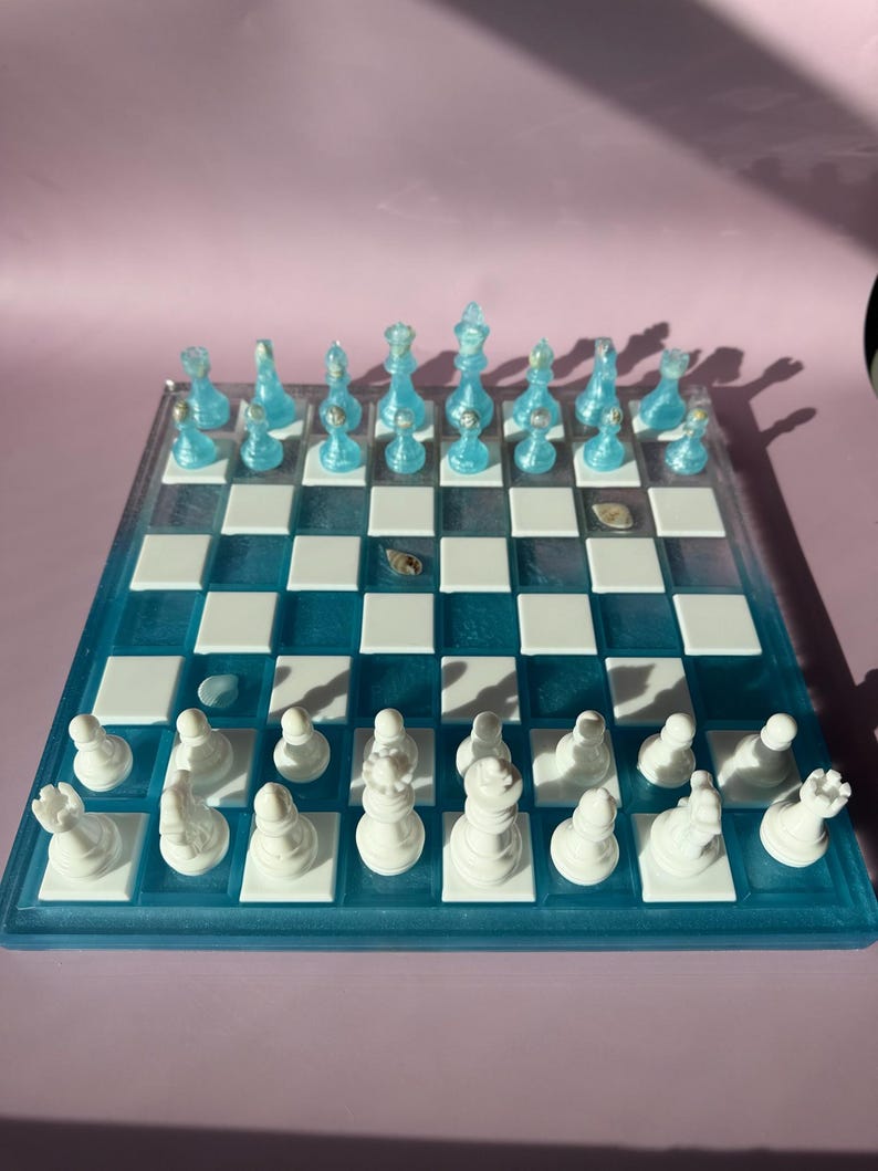 May include: A handcrafted chess set with a blue and white board. The chess pieces are white and blue. The board is square with alternating white and blue squares. The chess set is a unique and decorative item.