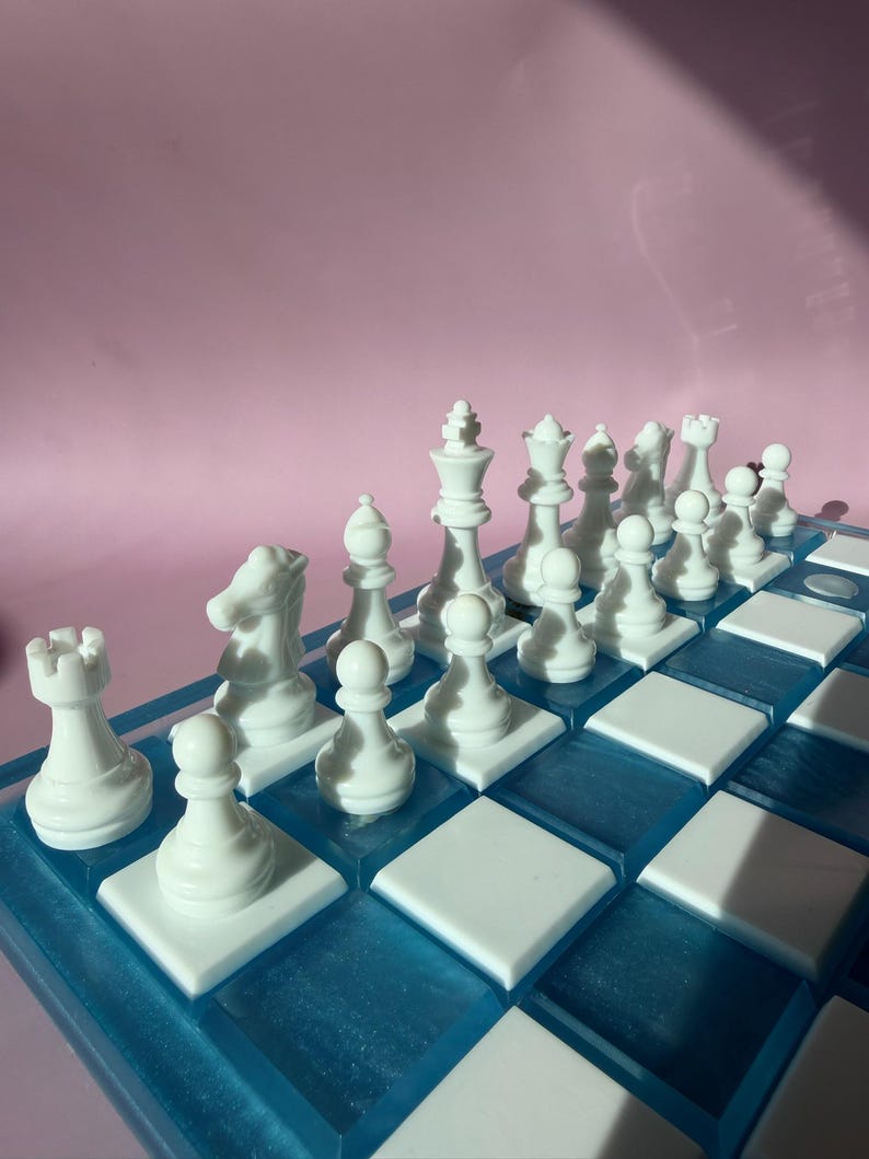 May include: A complete chess set with white pieces arranged on a blue and white checkered board. The pieces include pawns, rooks, knights, bishops, a queen, and a king. The board has a blue resin border and white squares.