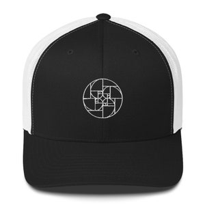 May include: A black and white trucker hat with a white embroidered geometric design on the front. The hat has a black front panel and a white mesh back panel.