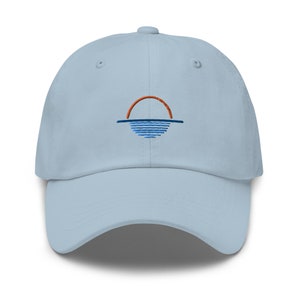 May include: A light blue baseball cap with an embroidered design of a sunset over water. The sun is orange and the water is blue.