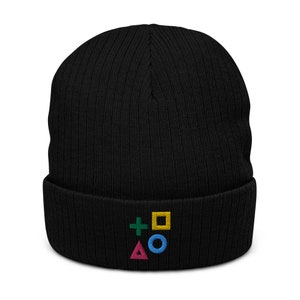 Peut inclure: Bonnet en tricot noir avec un symbole de manette de jeu PlayStation brodé en couleur. Le symbole comprend un signe plus vert, un carré jaune, un triangle rose et un cercle bleu.