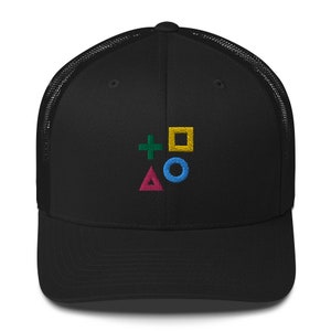 Peut inclure: Casquette de camionneur noire avec un dos en mesh noir. Le devant de la casquette présente un motif brodé des symboles de la manette PlayStation : un cercle, un triangle, un X et un carré.