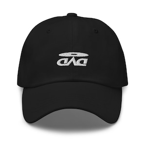 Può includere: Un cappello da baseball nero con un logo ricamato bianco di un disco con le lettere "DAD" all'interno.