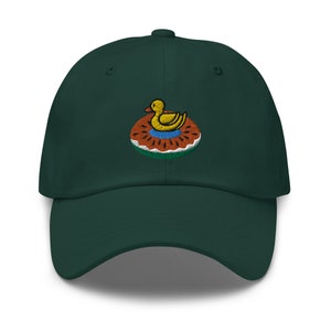 May include: A dark green baseball cap with a curved brim. The cap features an embroidered design of a yellow duck floating in a blue pool on a watermelon float. The watermelon float has a red rind with white and green accents.